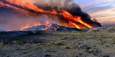 Intense wildfire raging across dry grassland during dramatic sunset skies photo