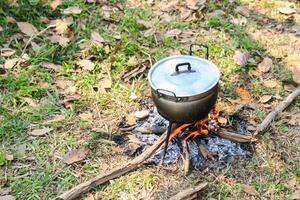 An aluminum pot sits atop a sturdy three legged iron stand, heated by an open fire. This time honored cooking technique is widely used for preparing meals in rural and outdoor settings. photo