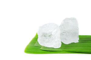 4. Pieces of white alum sit on banana leaf, set against a white background. This simple yet meaningful display represents the use of natural minerals in purification, skincare, and household remedies. photo