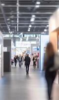 Blurred crowd walking inside a large hall with exhibition booths and modern architecture photo