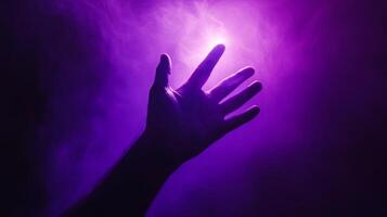 Mystical Reach A hand reaching toward a source of luminescent purple light in darkness photo