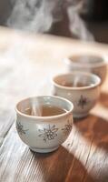 Gentle warmth emanating from a trio of floral patterned tea cups on rustic wooden surface photo