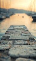 Stone pathway stretching into a serene harbour with boats and golden sunset light photo
