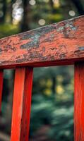 Weathered charm, red painted railing with peeling surface against verdant defocused woodland photo