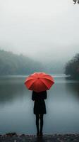 Woman with an orange umbrella stands by a foggy lake surrounded by trees in autumn. photo