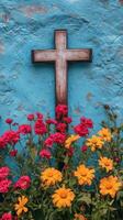 Colorful flowers and cross against a vibrant blue wall in a serene outdoor setting. photo