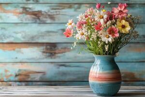 Fresh floral arrangement in a colorful vase on a rustic wooden table against a weathered blue background. photo