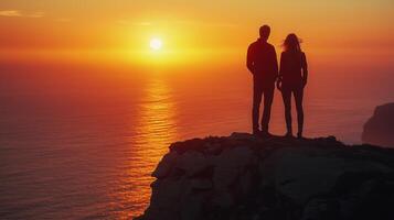 Couple gazes at stunning sunset over ocean from rocky cliff top. photo