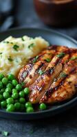 Grilled chicken breast served with mashed potatoes and peas on a black plate. photo