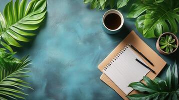 Working space with notepad, pens, coffee, and tropical plants on a blue desk. photo