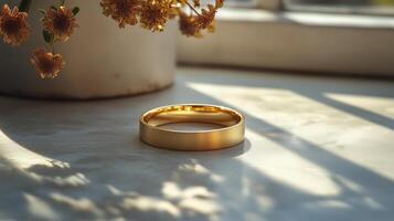 Golden wedding ring on a table with soft sunlight and dried flowers. photo