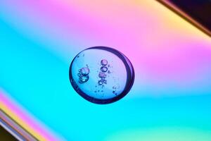 A drop of cosmetic serum on a multicolored background in shades of blue and lilac. photo