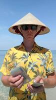Man in Vietnamese hat counting Vietnamese Dong bills on exotic beach in Vietnam video