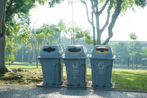 Trash bins in park with clear recycling instructions, surrounded by greenery and trees, promoting environmental awareness and cleanliness photo