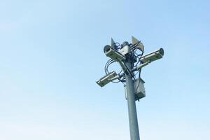 Surveillance camera tower with multiple cameras and antennas against clear blue sky. This structure is essential for monitoring and security in urban areas photo