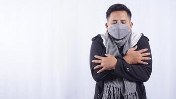 Sick Asian Man Wearing Mask and Scarf Shiver Severely on White Background photo
