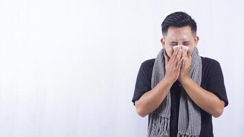 Asian Man Suffering from Flu Blows His Nose with Tissue Paper on White Background photo