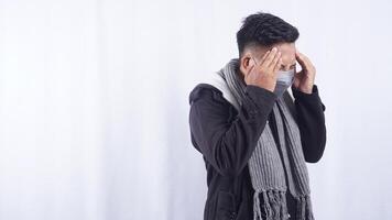 Side View of Asian Man Wearing Jacket, Scarf, and Mask Suffering from Bad Headache on White Background photo