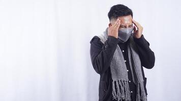Sick Asian Man Wearing Jacket, Scarf, and Mask Suffering from Bad Headache on White Background photo