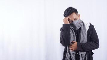 Asian Man Wearing Jacket, Scarf, and Mask Touching Head Suffering from Bad Headache on White Background photo