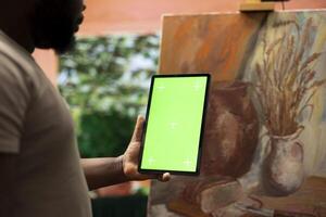 African american painter using a gadget with copy space screen in workshop, working on his new nature inspired masterpiece on canvas. Using watercolor paint and creativity in atelier. photo