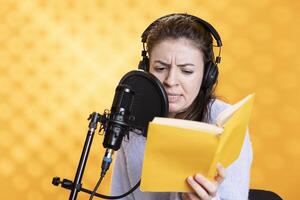 Narrator frowning while reading book, recording audiobook using microphone, playing angry character, studio background. Woman producing digital recording of novel, interpreting furious antagonist photo
