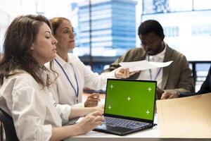 CEO uses laptop with green screen during a meeting with business associates, reviewing project development progress. Utilizing detailed analytics and mockup to ensure strategic objectives. photo