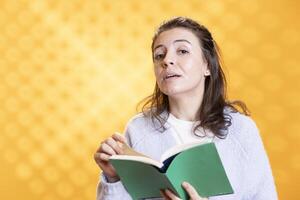 Portrait of woman turning page on book, enjoying reading hobby for relaxation purposes. Bookaholic person with novel in hands enthralled by story, isolated over studio background photo