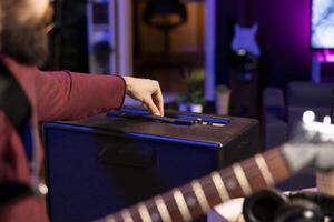 Sound engineer adjusting volume levels on his amplifier to record acoustic guitar tunes for editing session in music post production. Male producer composing a new song in home studio. Close up. photo