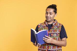 Indian man reading book, having fun and enjoying characters and plot, isolated over studio background. Relaxed person browsing novel, enjoying leisure time, appreciating literature photo