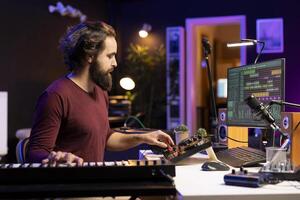 Sound engineer mixing and mastering new songs in home studio, adding piano electronic keyboard tunes. Young talented producer composing music with stereo equipment and synthesizer. photo