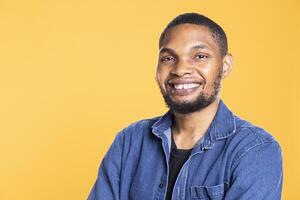 Portrait of charming cool african american man posing on camera, standing with arms crossed against yellow background. Relaxed confident person in a good mood smiling in studio. photo