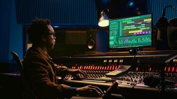 African american sound designer working with editing software to produce new tracks. Audio engineer uses mixer and compressor, changes volume level and sound settings in post production. Camera B. photo