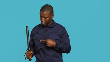 Portrait of security agent removing baton from belt, using it to secure assigned post, studio background. African american guardian pointing finger to truncheon, handling security breaches, camera A photo
