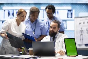 Group of doctors consulting hospital records next to chroma key display, using x ray test results to examine the diagnosis. Diverse experts meeting at private clinic to provide a treatment plan. photo