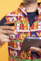Focus on debit card used by man in blurry background adding payment method on shopping website using tablet. Close up shot of person buying stuff online using credit card, typing data on device photo