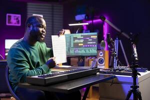 Artist pointing at musical sheet notation to explain notes on piano, teaching people to play synthesizer in home studio. Famous composer musician playing midi controller during online master class. photo
