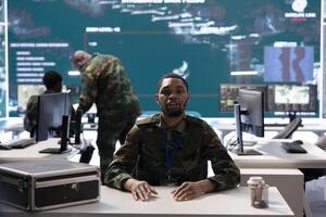 Army soldier in a high tech monitoring room conducts a videocall, leveraging secure communication channels and real time intelligence for effective mission coordination. National defense activity. photo
