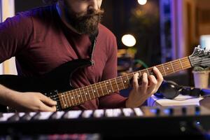 Musical artist playing acoustic guitar and recording a new song in home studio, using modern acoustical engineering tools. Composer creating new audio sounds on instrument, post production. photo