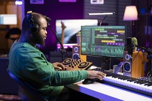 Sound producer operating on mixing console and piano keys in home studio, editing his audio recorded files on DAW software. Recording expert enhancing quality on old recordings. photo