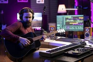 Artist recording his acoustic guitar tunes in home studio, using daw software interface on computer. Composer playing new string accords on musical instrument, acoustical engineering. photo