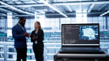 Focus on laptop in data center with artificial intelligence brain used by engineers in blurry background. Close up of device displaying AI deep learning software in server farm, camera B photo