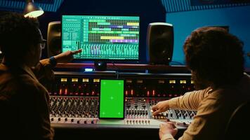 Diverse music experts working with greenscreen on tablet and mixing console in control room, pressing key buttons and pushing sliders. Artist and producer creating a hit song in studio. Camera B. photo