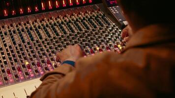 Audio technician producing new music at mixing console in control room, twisting knobs, pressing sliders and switchers. Producer working on processing and editing sounds quality. Camera B. photo