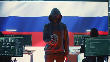Digital outlaw hacker in a dark hood issuing cyber threats with a human skull to make death threats, aggressive malicious intent. Russian man committing cybercrime and scamming nations. Camera B. photo
