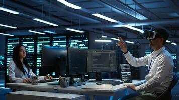 Data center admin responsible for installation of networking systems wearing high tech VR headset. IT worker doing maintenance on server farm gear using virtual reality technology, camera B photo