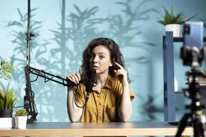 Internet star recording channel intro for digital platforms, talking into high quality microphone, discussing with social media followers. Female influencer setting up equipment for viral photo