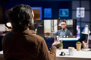 Focus on cybersecurity specialist helped by african american coworker in blurry background on computer monitor during internet videocall meeting to look for company security vulnerabilities photo