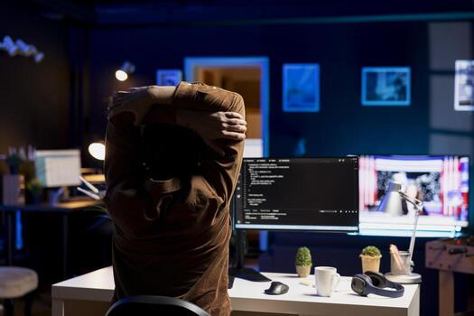 Programmer doing software quality assurance, stretching arms behind back after reading source code, feeling fatigued. IT expert taking break from work to relax muscles after inspecting coding photo