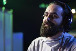 Smiling man relaxing by playing science fiction FPS videogame with friends on PC at computer desk at night. Close up of upbeat gamer communicating with teammates, shooting enemies in online shooter photo